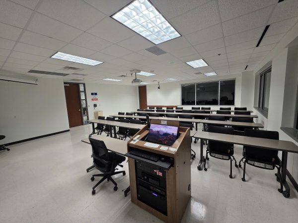 View from behind the instructor's desk looking out at the classroom, showing the monitor and integrated technology controls.