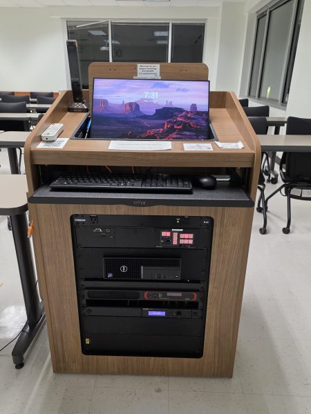 Detail view of a professional A/V rack inside a wooden lectern showing an Extron controller, Shure wireless receiver, and Dell micro-PC.